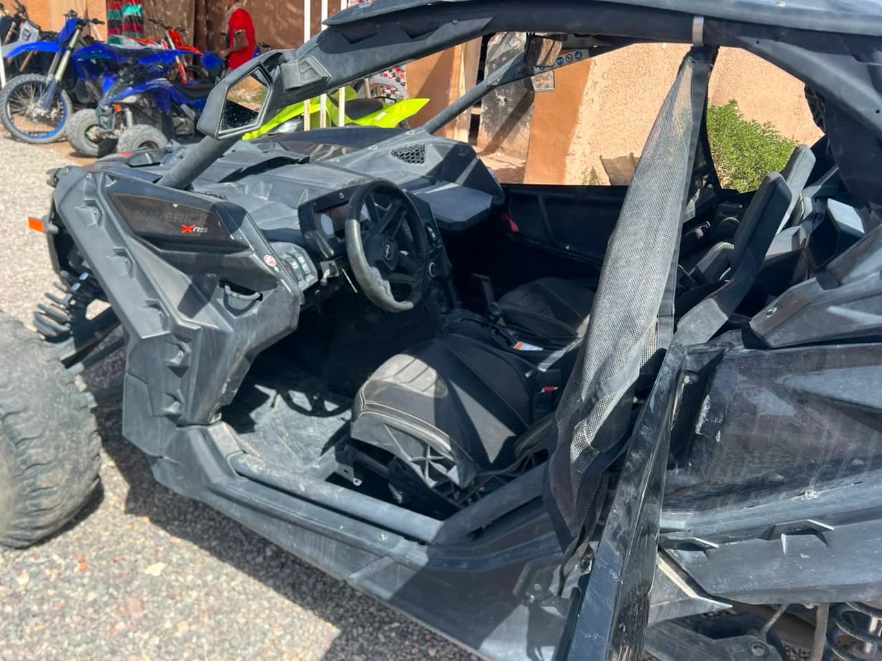Close-up of the Can-Am Maverick X3's dashboard and "MAVERICK X RS" badge, with other fleet vehicles visible behind