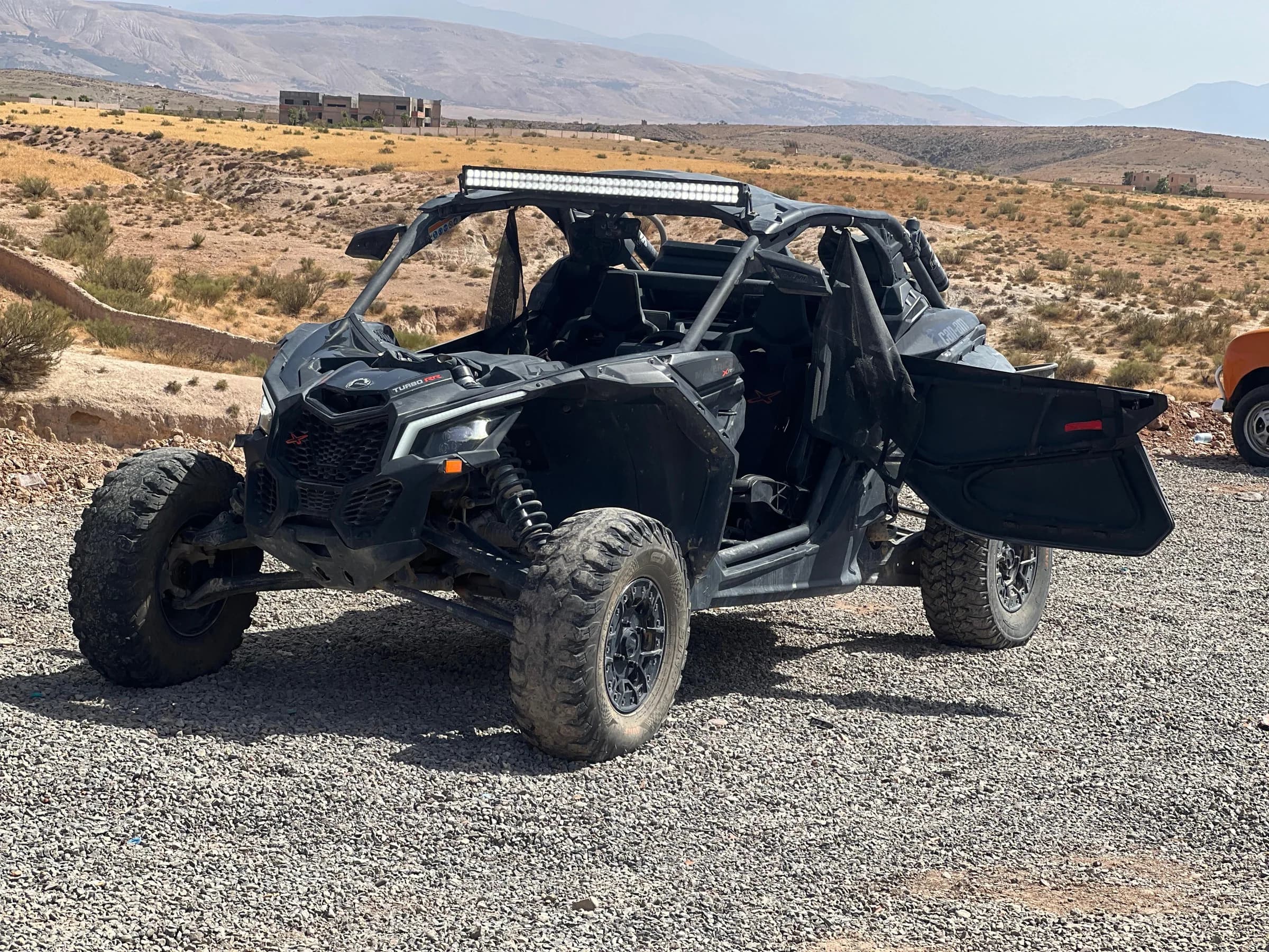 An off-road buggy parked with the dry, rocky mountains of the Agafay Desert behind it