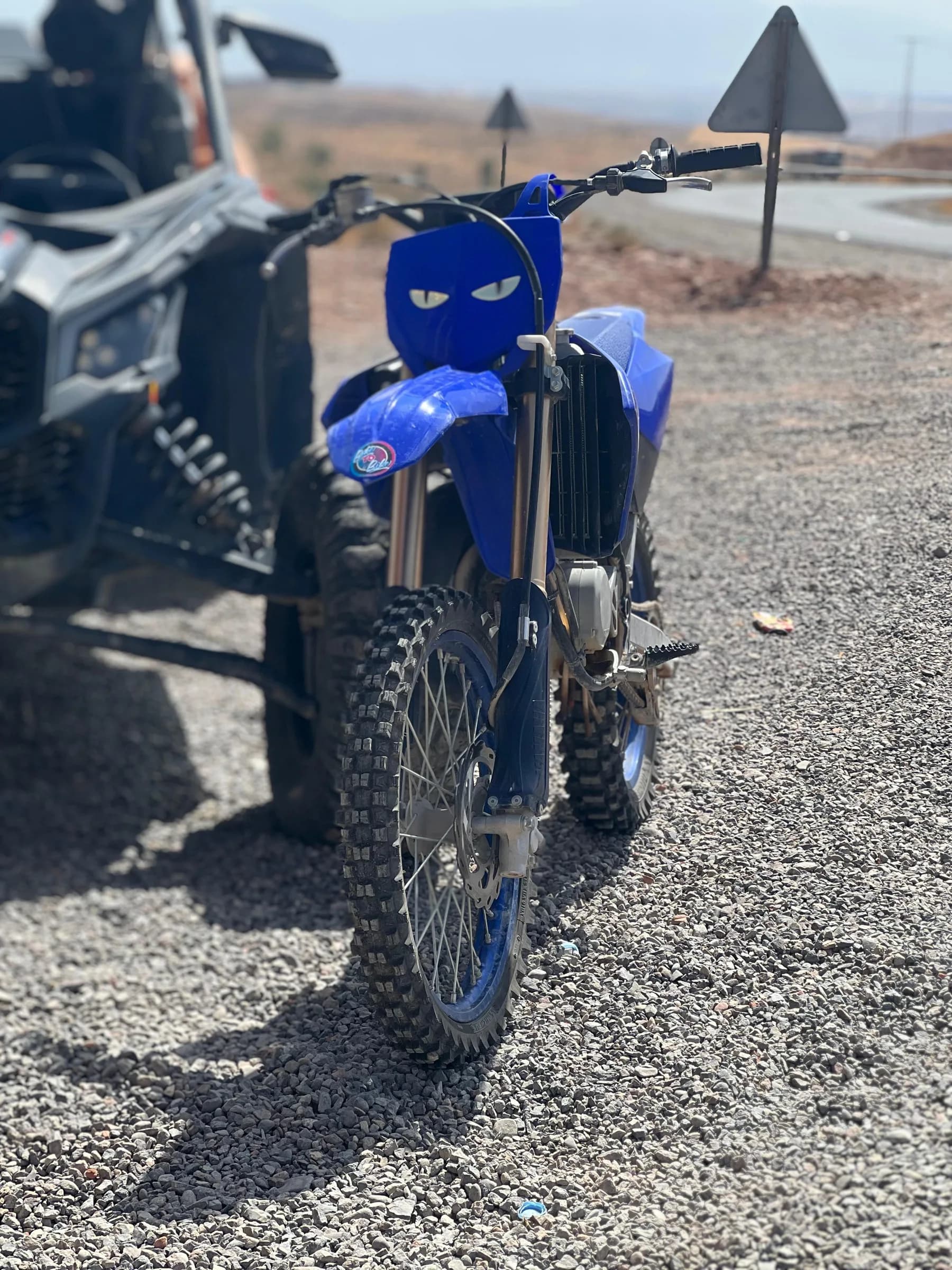 Front view of a blue dirt bike parked beside a road