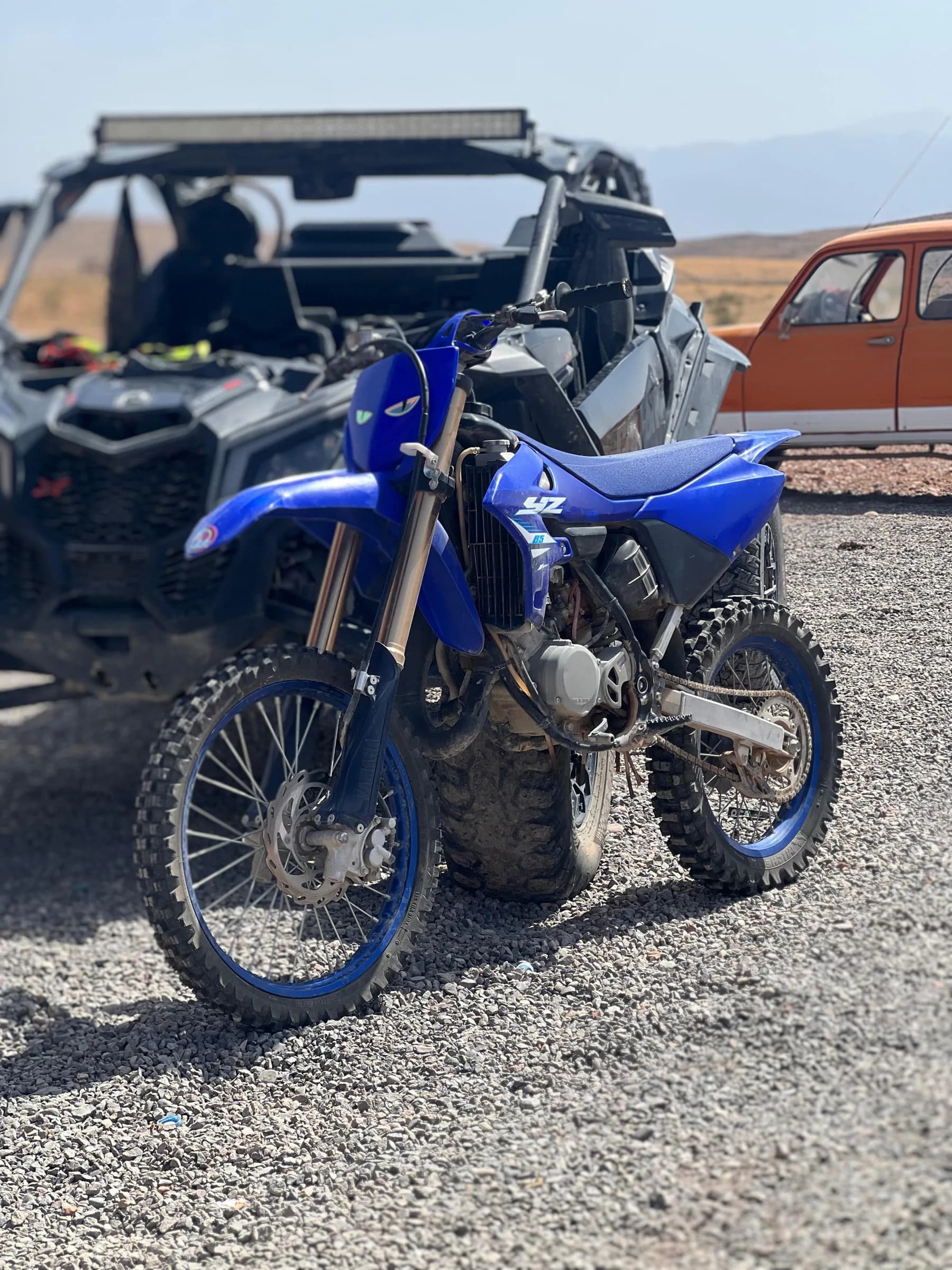 A blue Yamaha YZ dirt bike parked at the rental shop, with a buggy and a car in the background