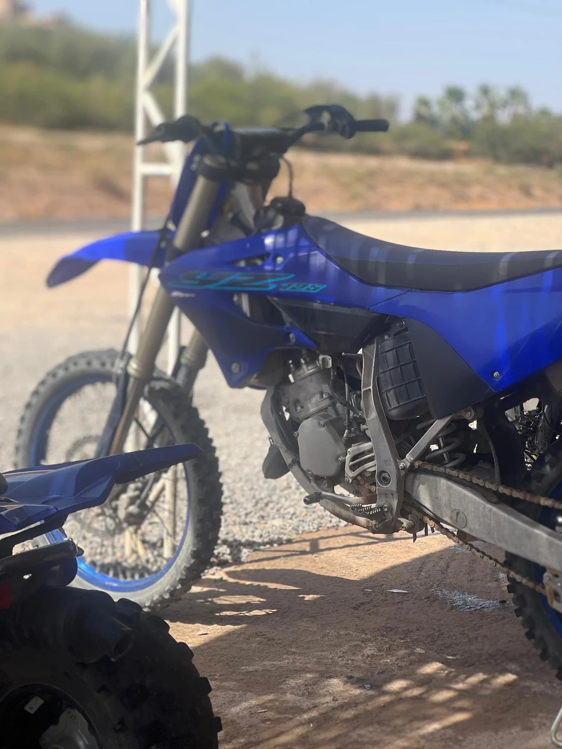 A blue dirt bike parked in a yard with trees nearby