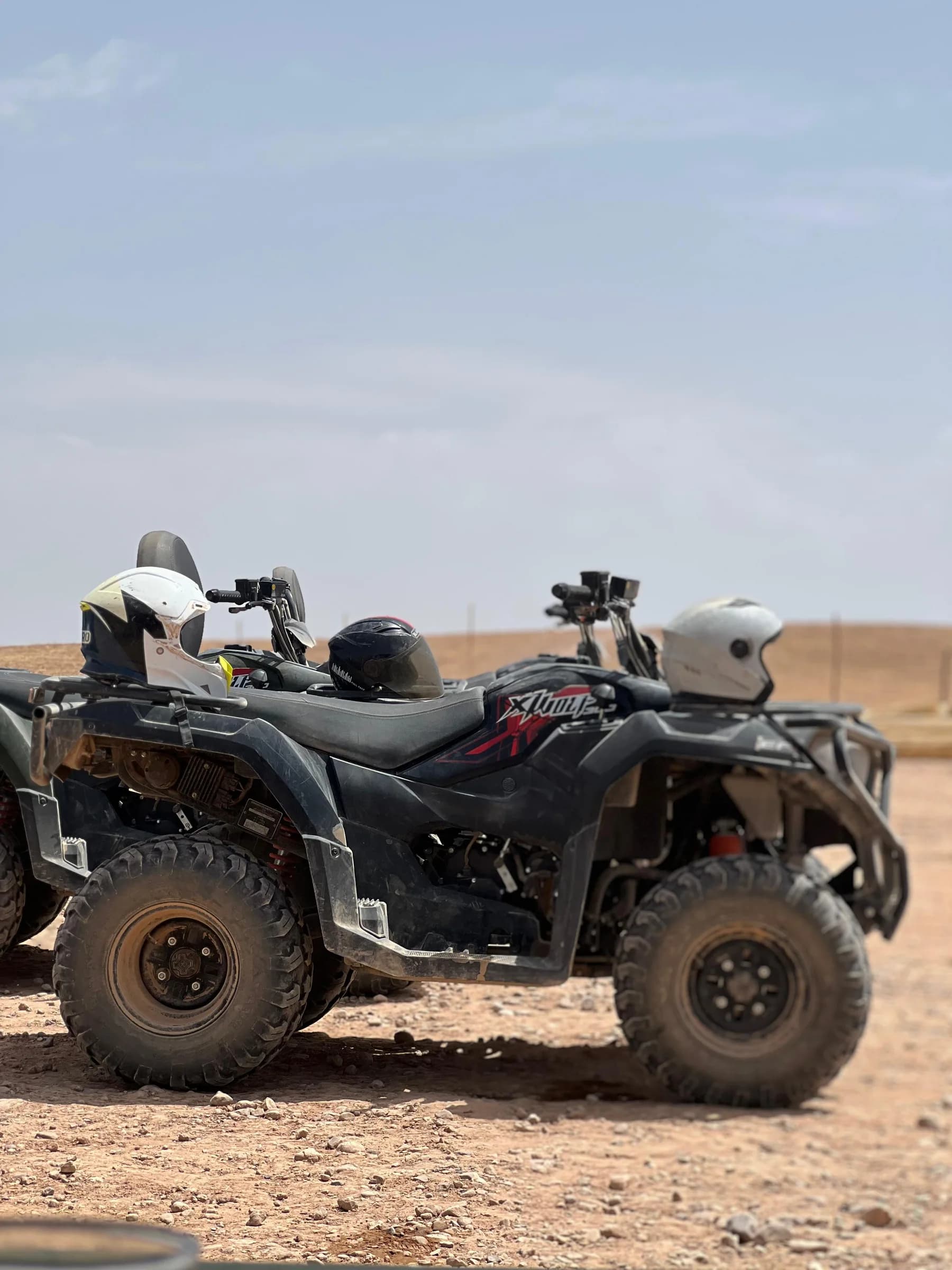 A black quad bike parked with dust and desert hills in the background