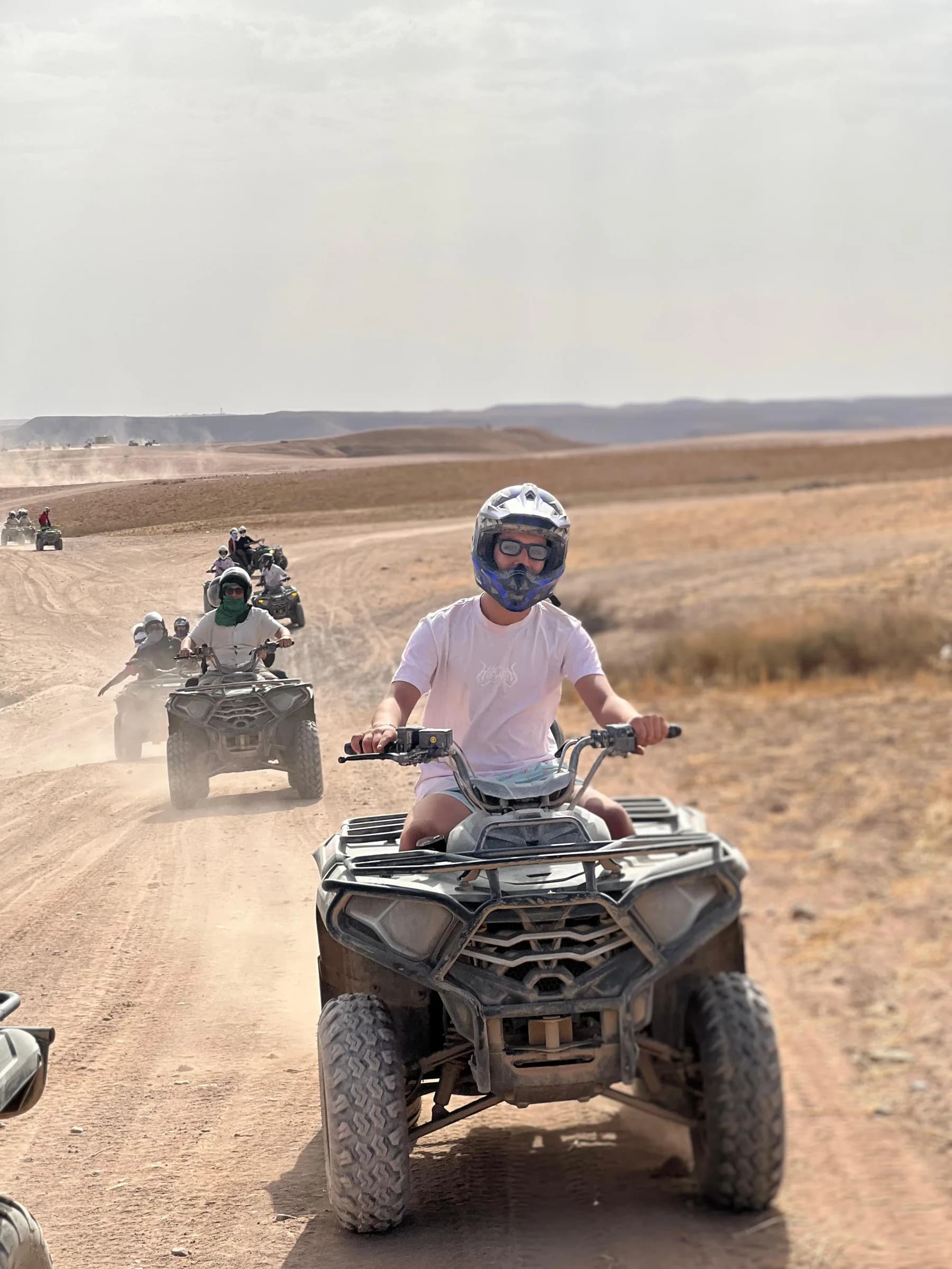 Quad bike riders on a desert road with dust trailing behind