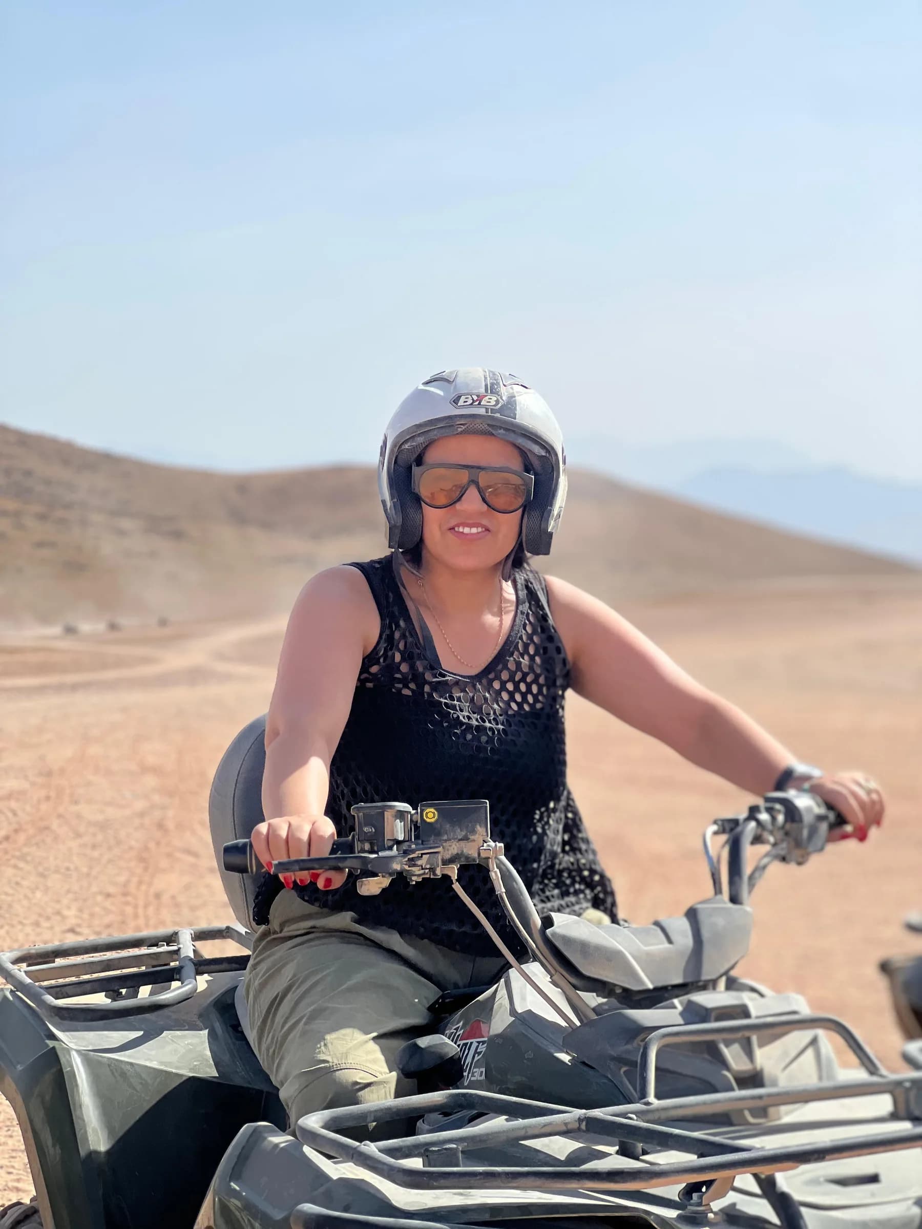 A woman wearing a helmet and sunglasses sitting on a quad bike