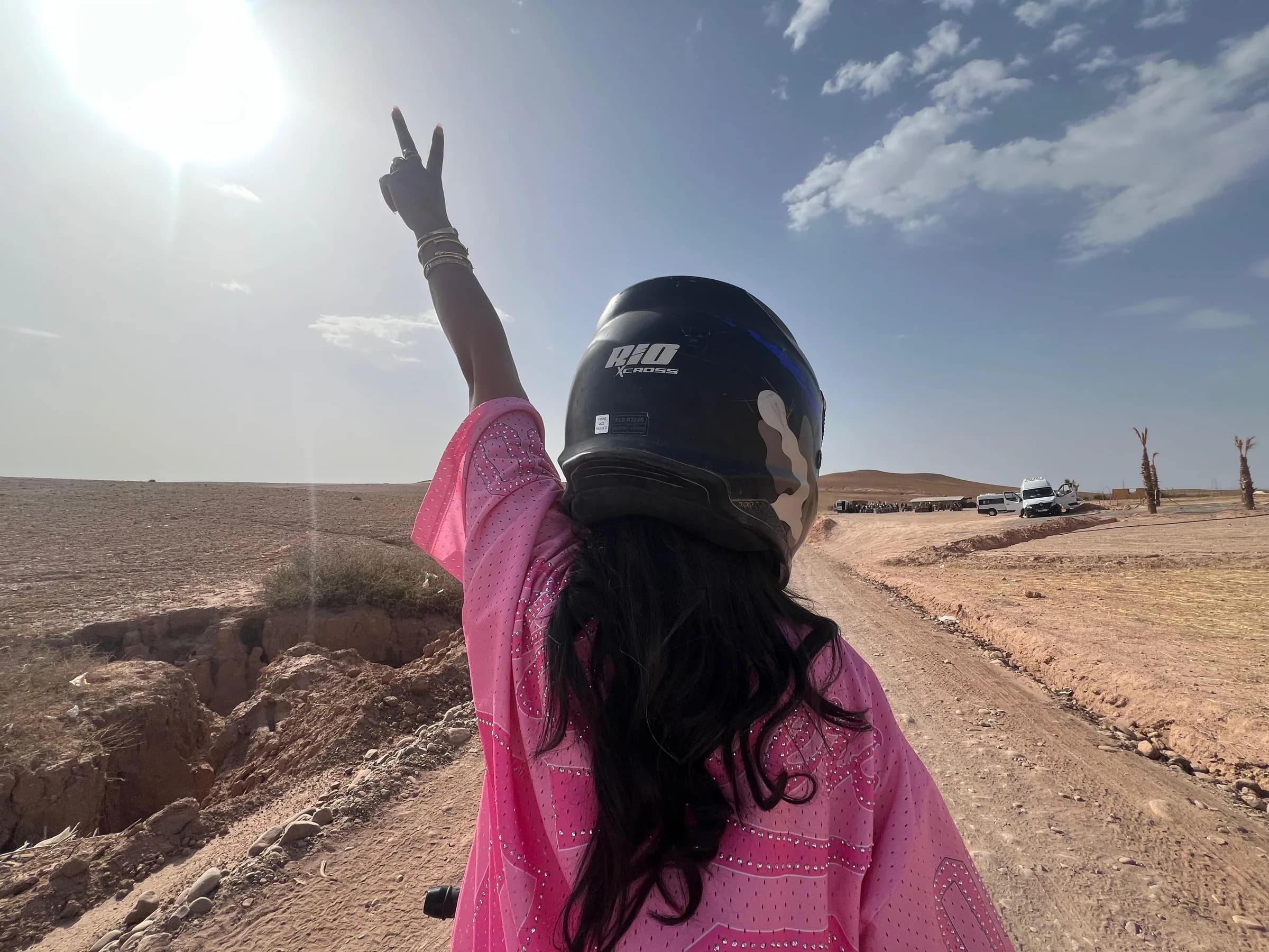A woman in a pink outfit and helmet raising her hand on a desert road